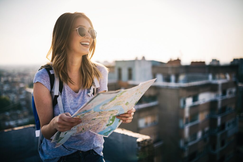 Giovane donna felice con una mappa della città e uno zaino che sorride.