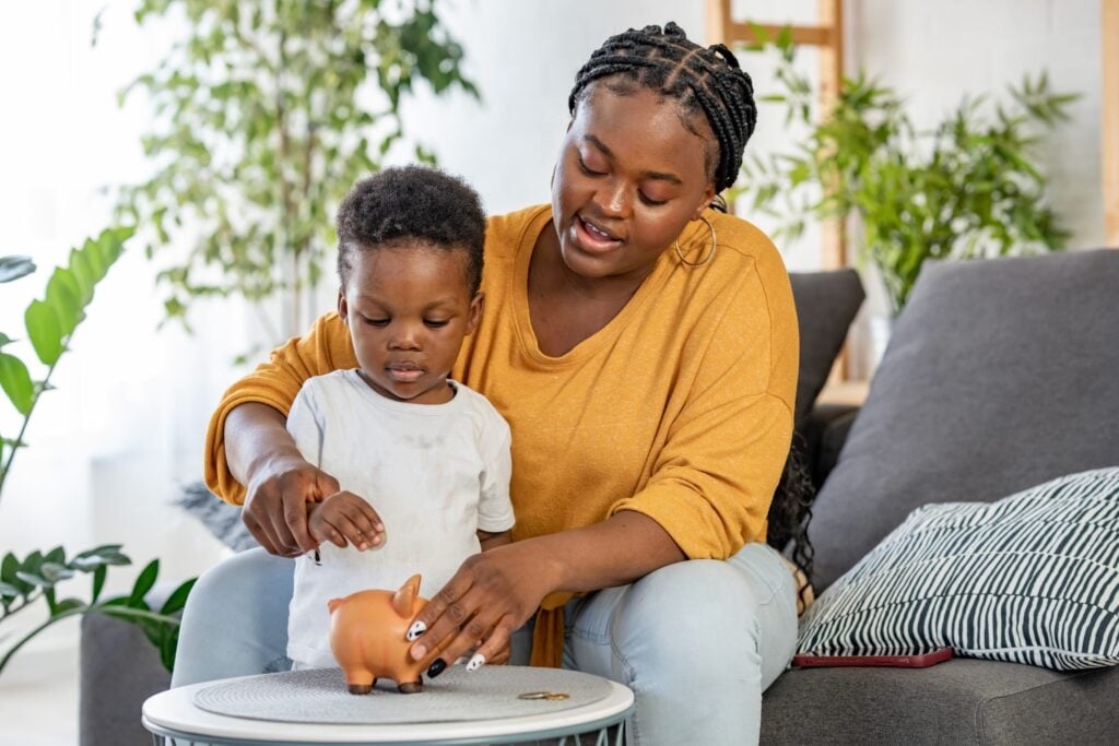 Bambino con sua madre che inserisce una moneta in un salvadanaio